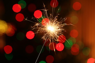 Photo of Bright burning sparkler on dark background with blurred lights, bokeh effect