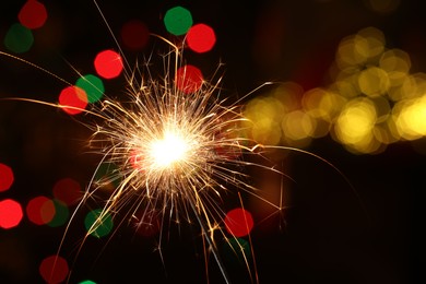 Photo of Bright burning sparkler on dark background with blurred lights, space for text. Bokeh effect