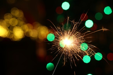 Photo of Bright burning sparkler on dark background with blurred lights, space for text. Bokeh effect