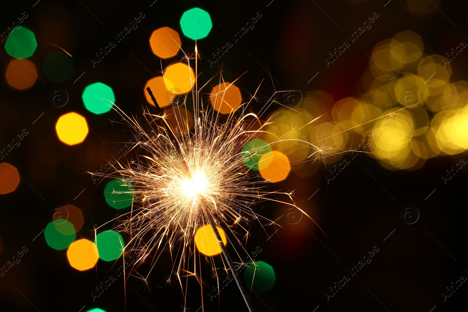 Photo of Bright burning sparkler on dark background with blurred lights, space for text. Bokeh effect