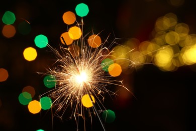 Photo of Bright burning sparkler on dark background with blurred lights, space for text. Bokeh effect