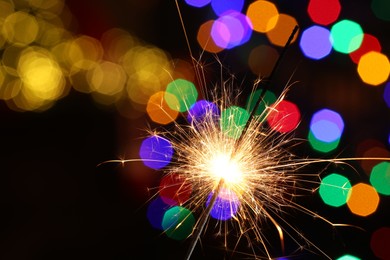 Photo of Bright burning sparkler on dark background with blurred lights, space for text. Bokeh effect