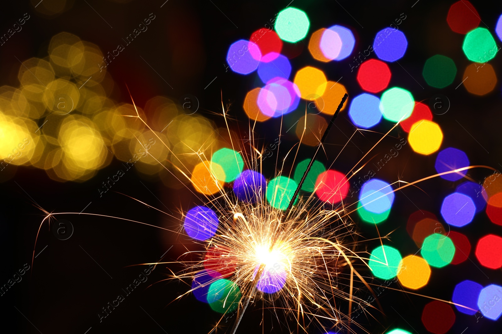 Photo of Bright burning sparkler on dark background with blurred lights, space for text. Bokeh effect