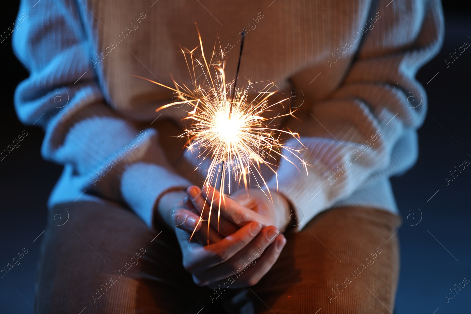 Photo of Woman with bright burning sparkler on dark background, closeup