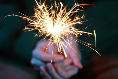 Photo of Woman with bright burning sparkler, closeup view