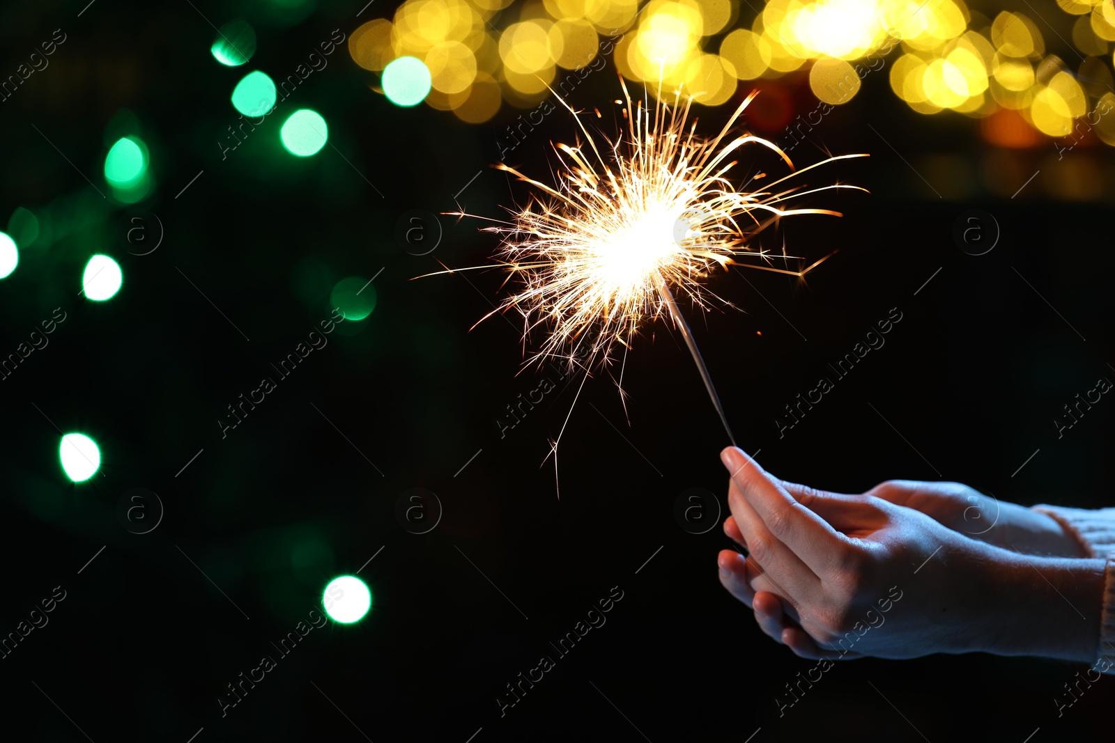 Photo of Man holding bright burning sparkler on dark background with blurred lights, closeup. Bokeh effect