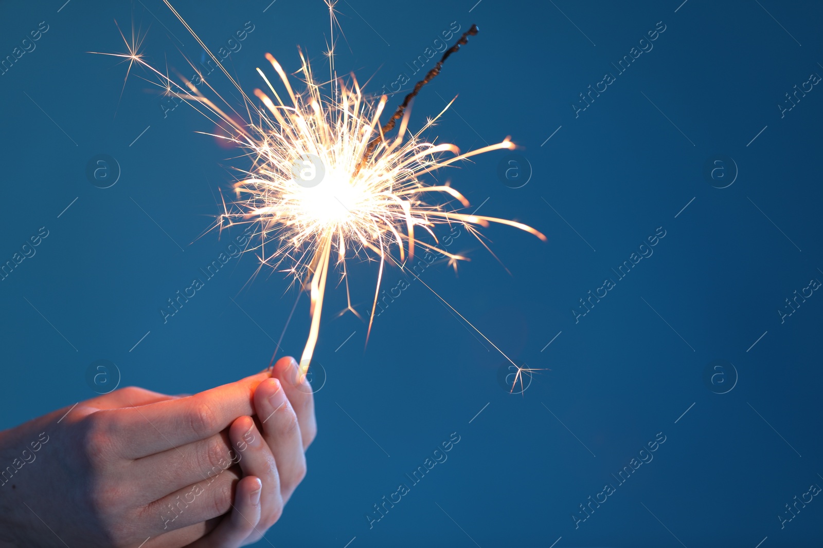 Photo of Man with bright burning sparkler on light blue background, closeup. Space for text