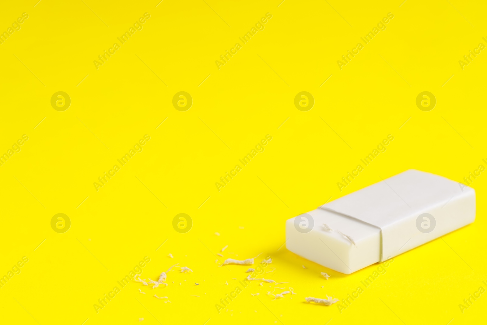 Photo of One eraser and scraps on yellow background, closeup. Space for text