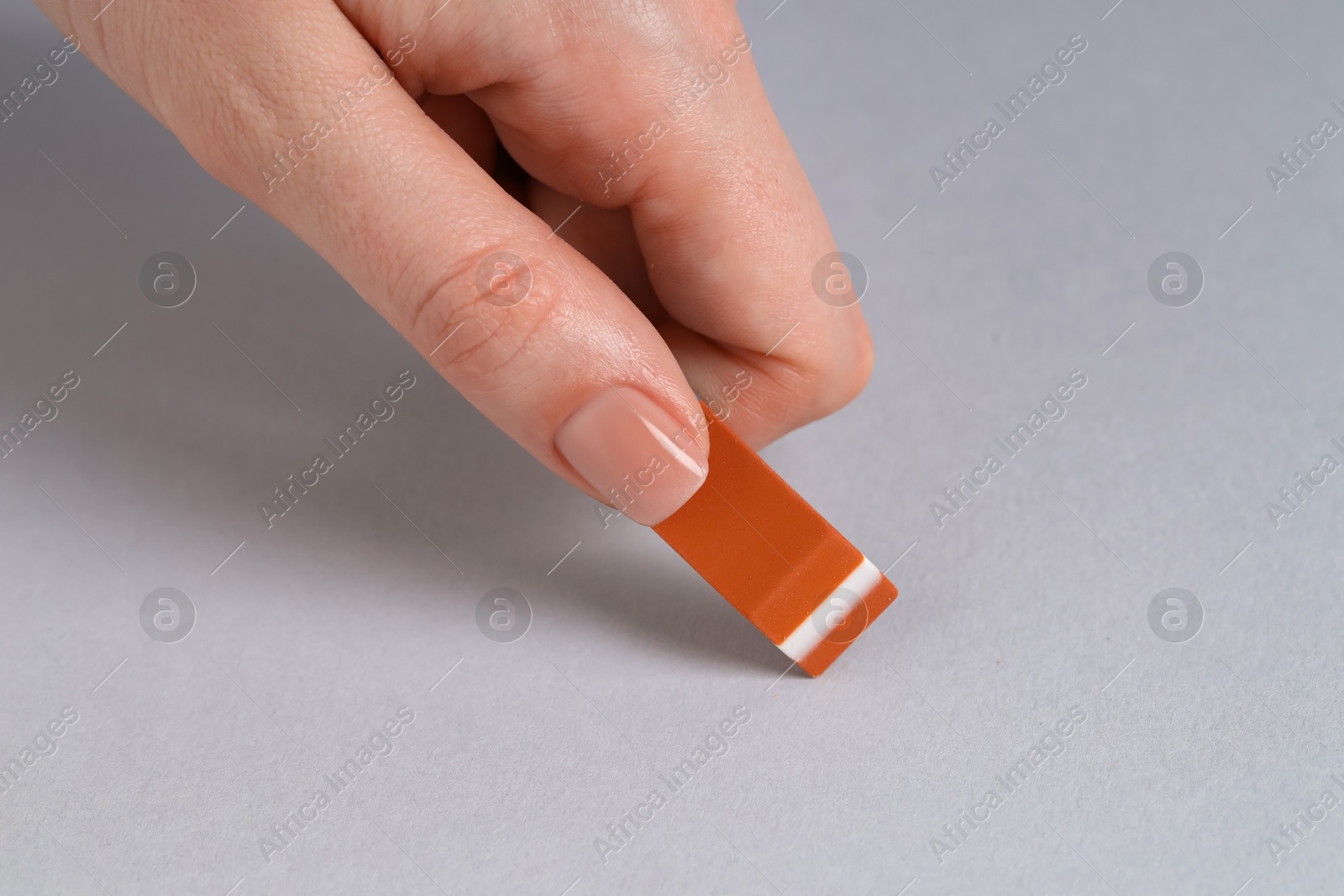 Photo of Woman using eraser on grey background, closeup