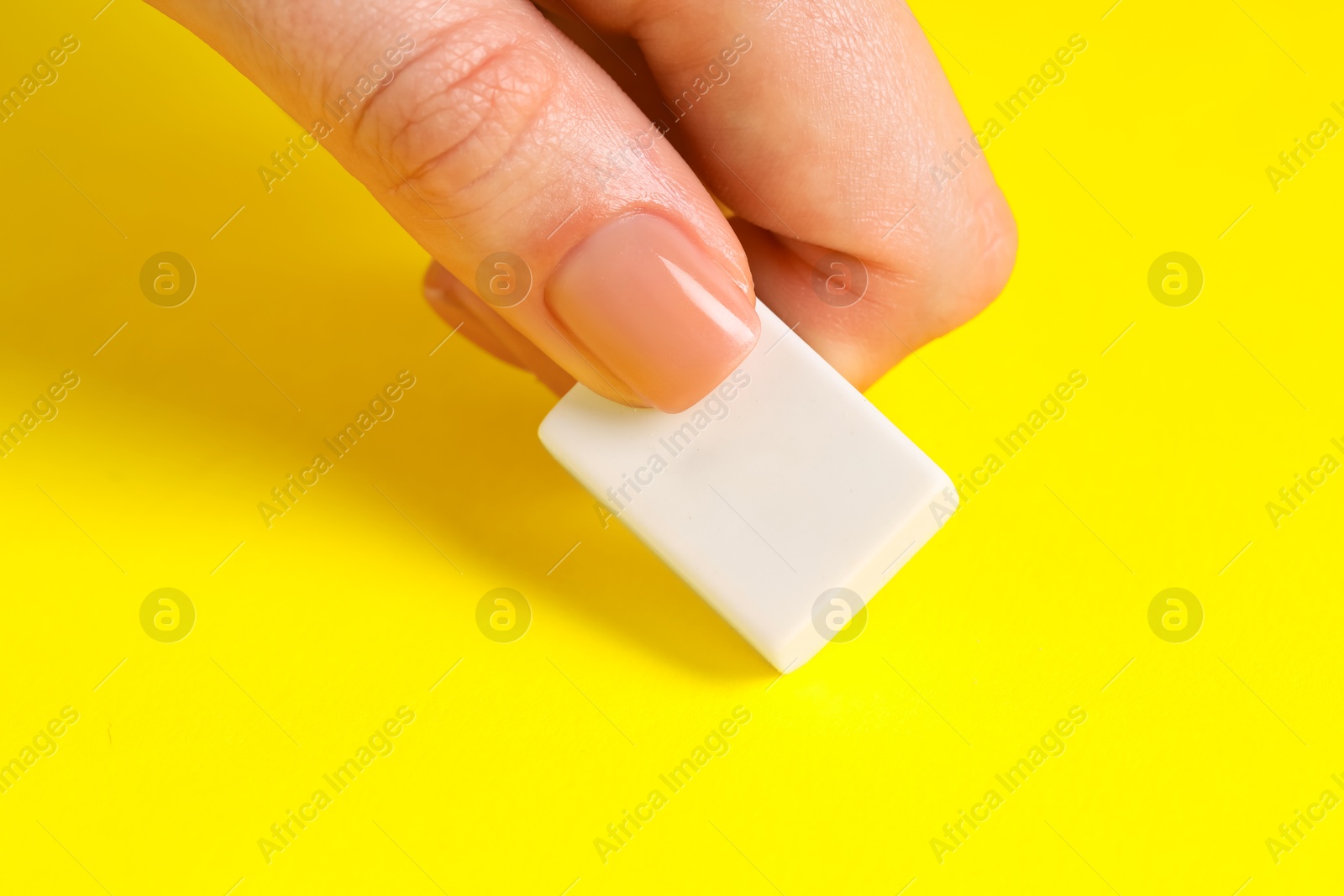 Photo of Woman using eraser on yellow background, closeup