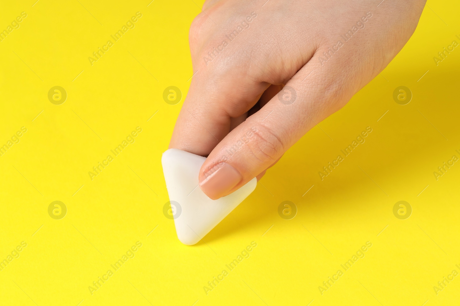 Photo of Woman using eraser on yellow background, closeup