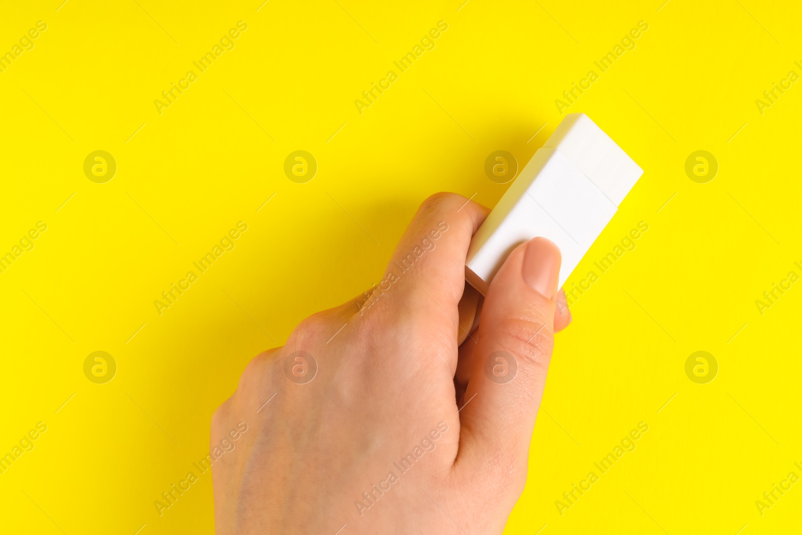 Photo of Woman using eraser on yellow background, closeup