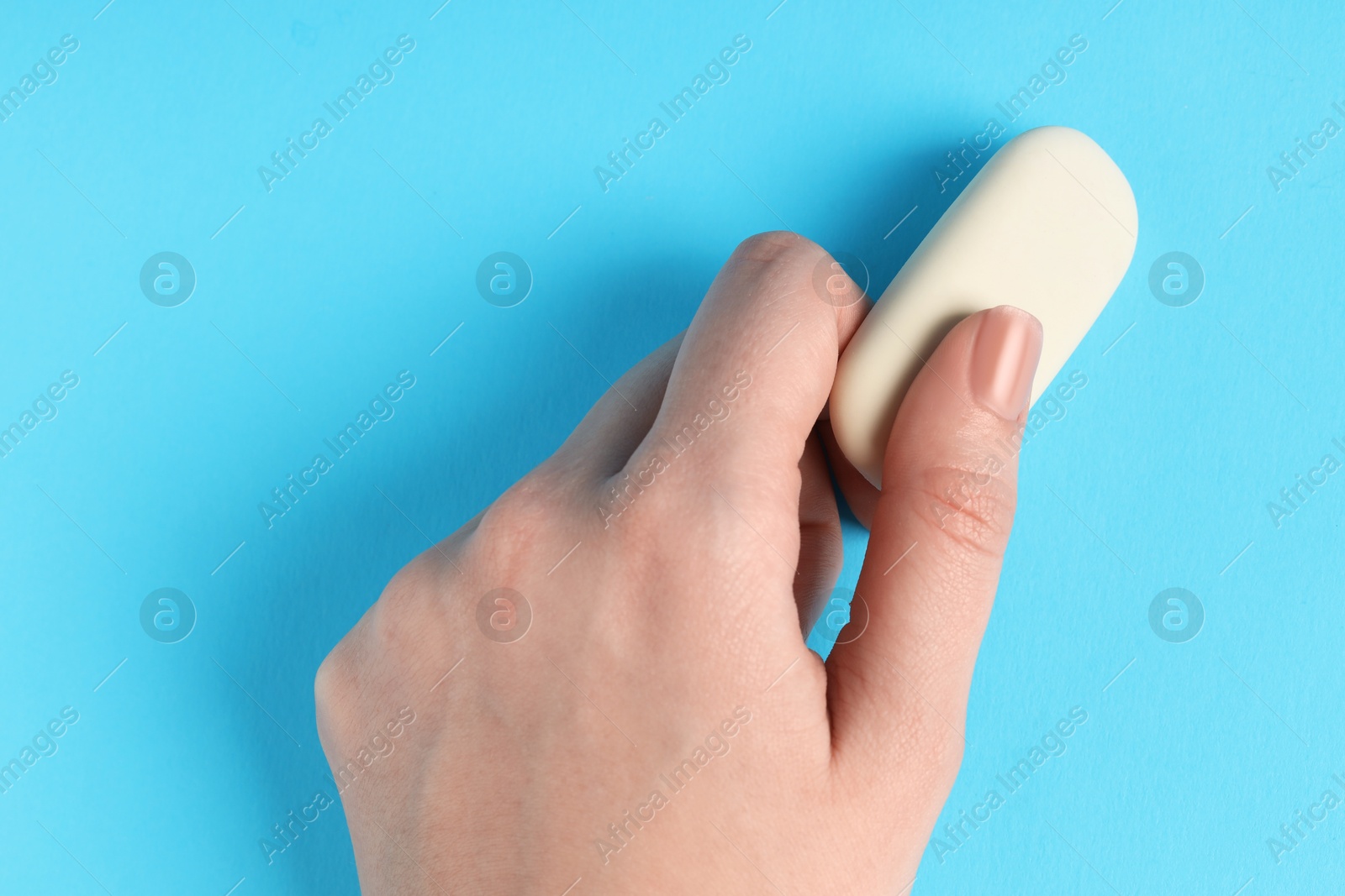 Photo of Woman using eraser on light blue background, closeup