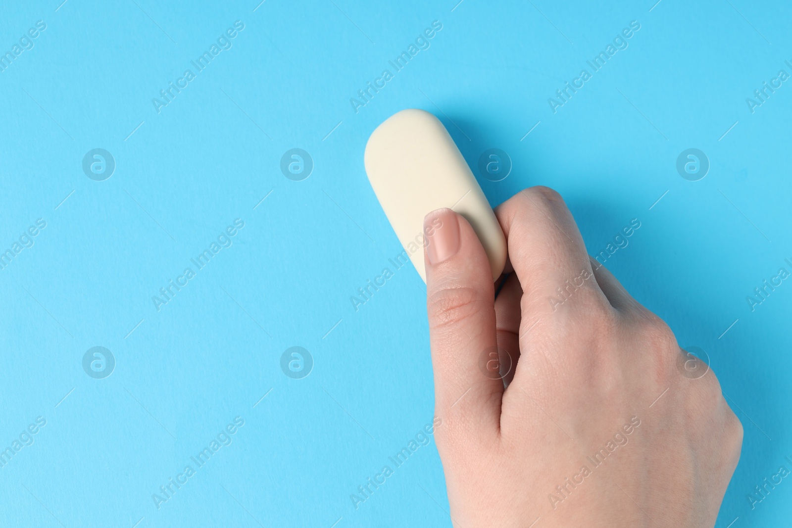 Photo of Woman using eraser on light blue background, closeup. Space for text