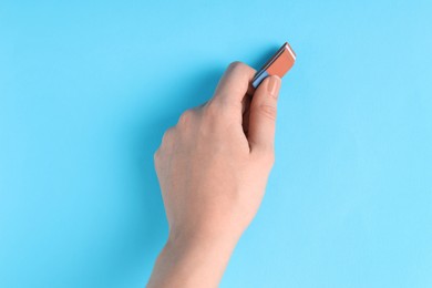 Photo of Woman using eraser on light blue background, closeup