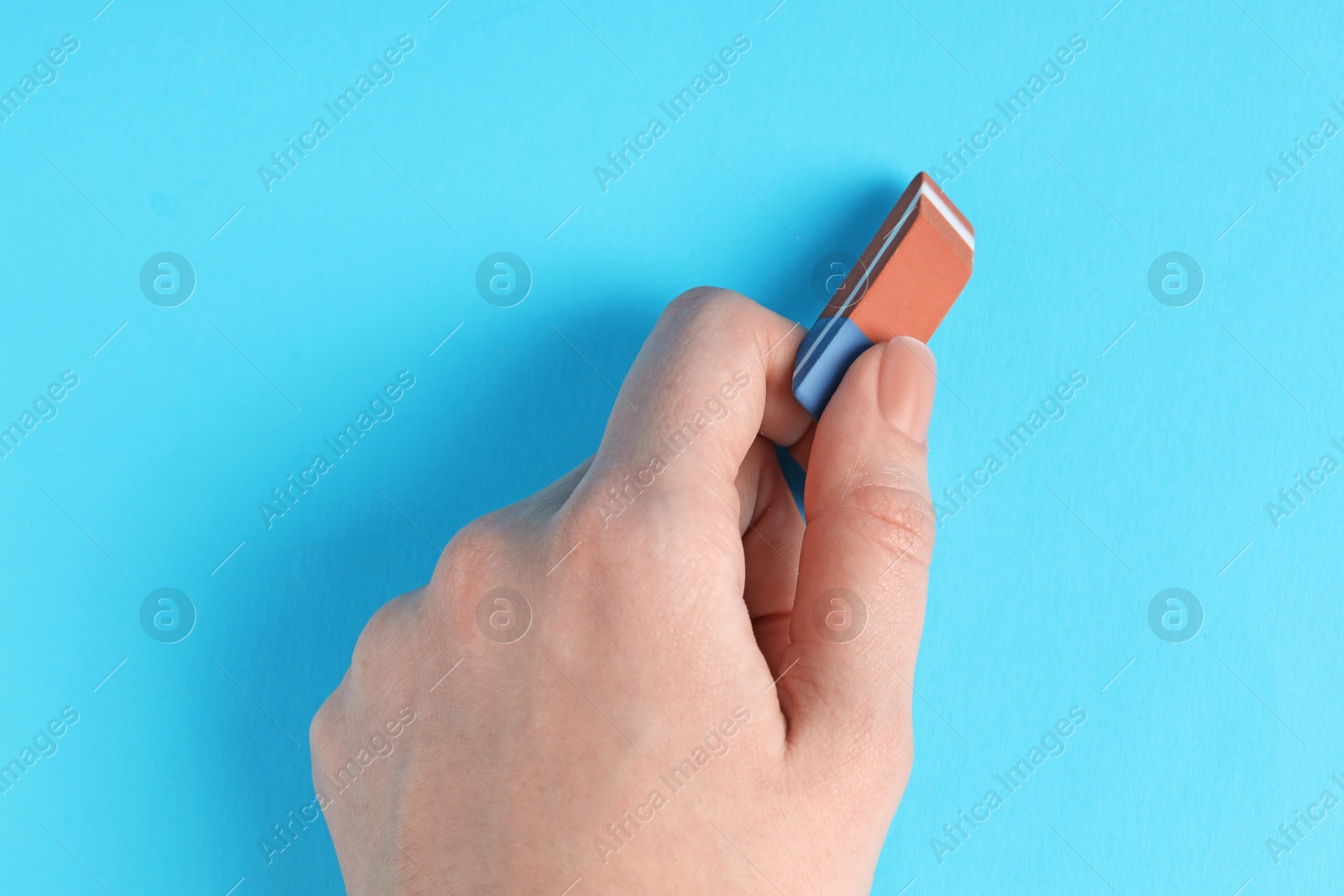 Photo of Woman using eraser on light blue background, closeup