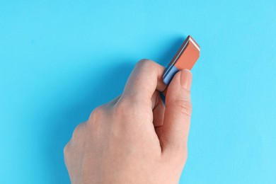 Photo of Woman using eraser on light blue background, closeup