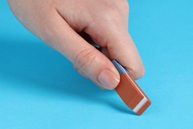 Photo of Woman using eraser on light blue background, closeup