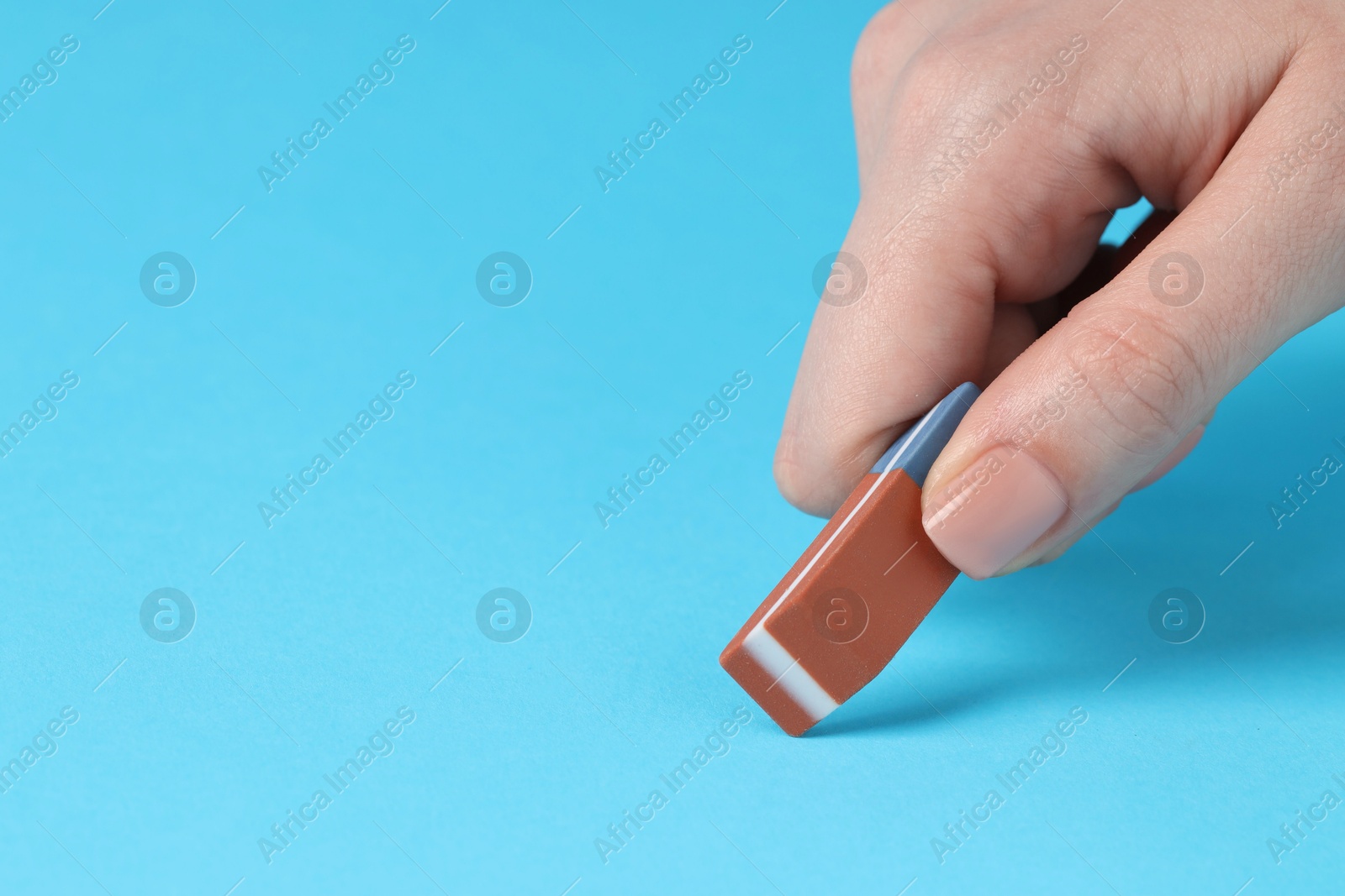 Photo of Woman using eraser on light blue background, closeup. Space for text