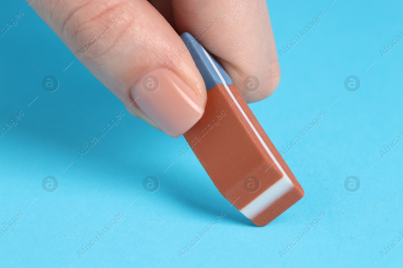 Photo of Woman using eraser on light blue background, closeup