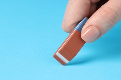 Photo of Woman using eraser on light blue background, closeup. Space for text