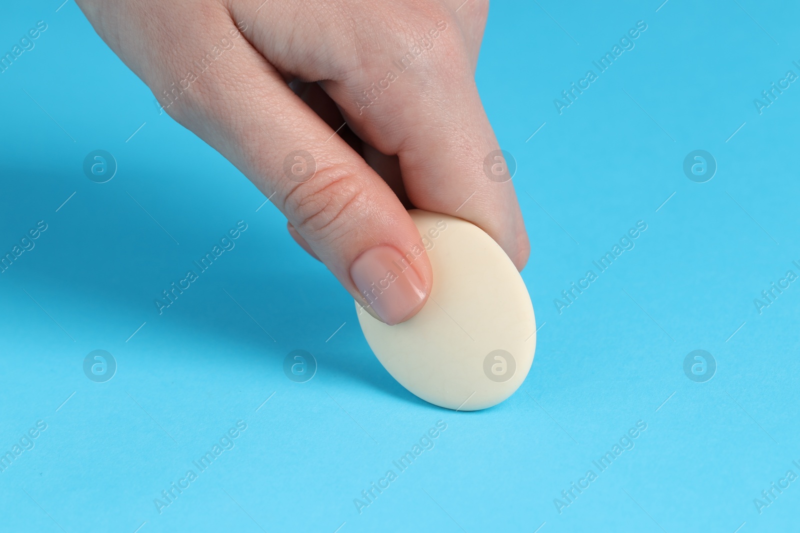 Photo of Woman using eraser on light blue background, closeup