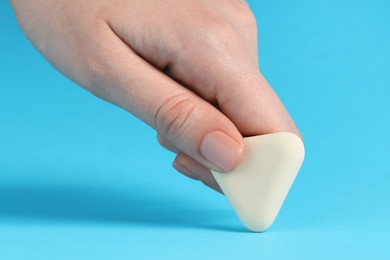 Photo of Woman using eraser on light blue background, closeup