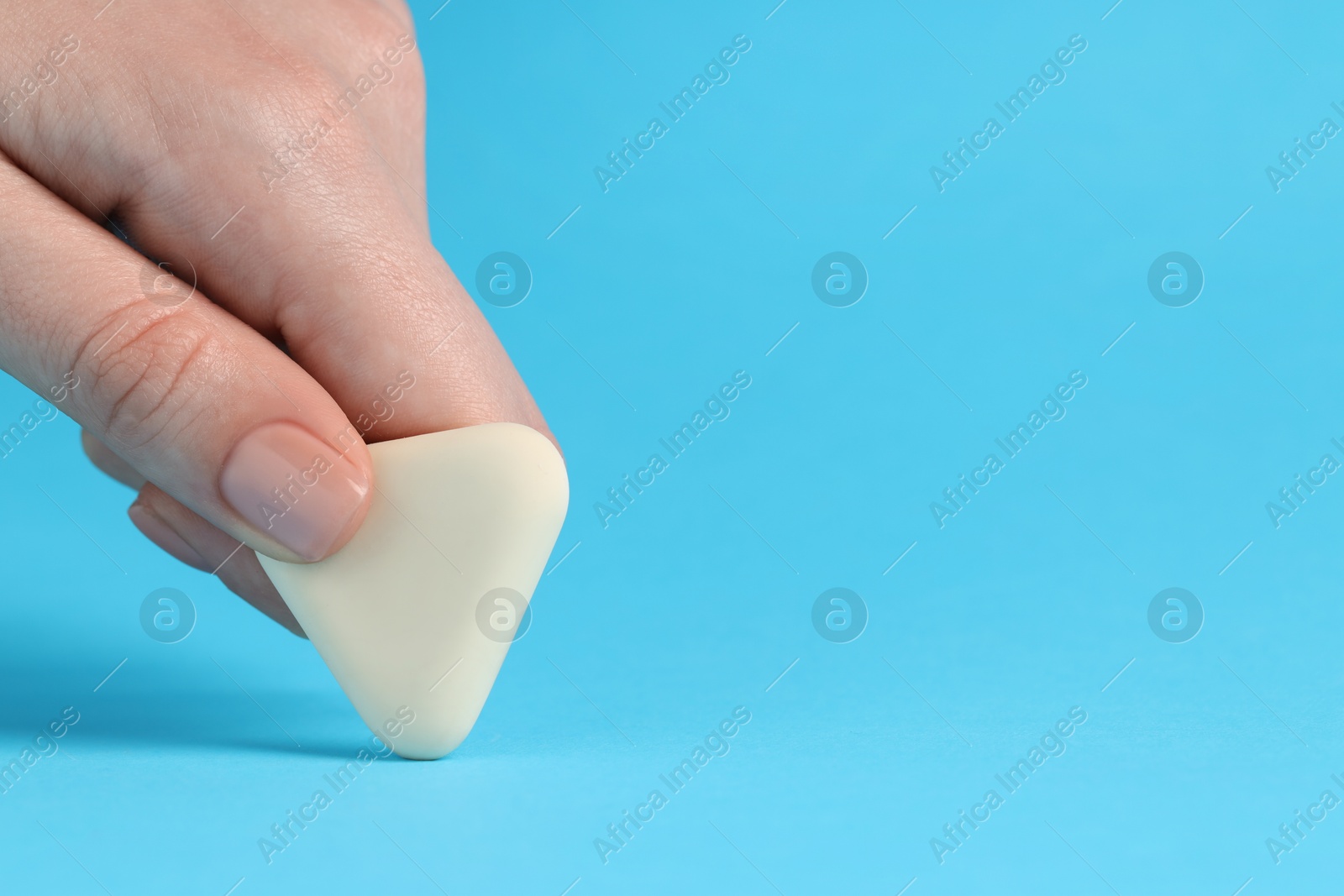 Photo of Woman using eraser on light blue background, closeup. Space for text