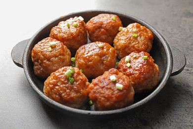 Photo of Tasty meatballs with green onion in baking dish on grey table, closeup