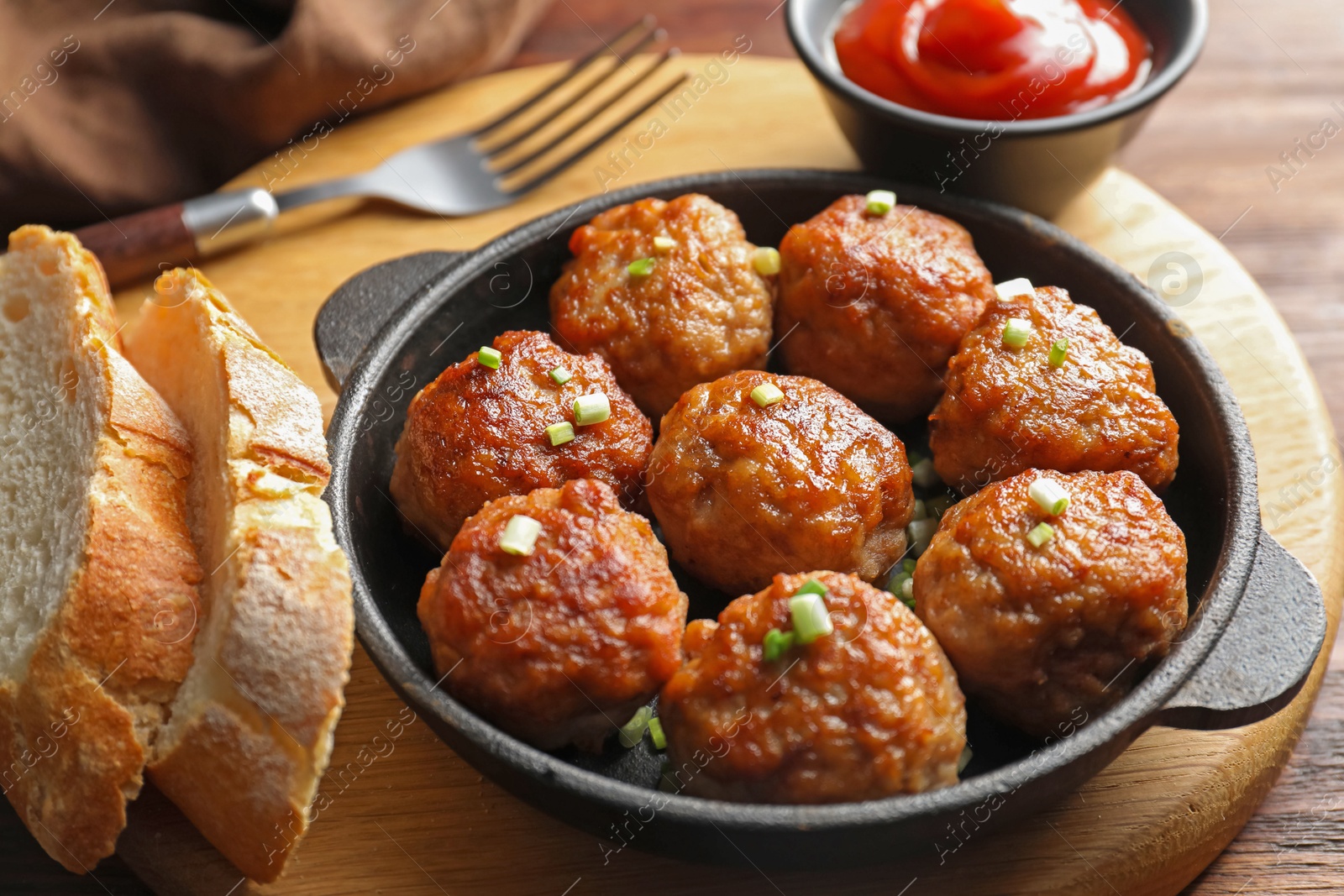 Photo of Tasty meatballs with green onion in baking dish served on wooden table