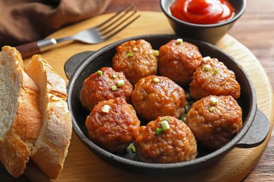 Photo of Tasty meatballs with green onion in baking dish served on wooden table