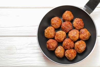 Photo of Tasty meatballs in frying pan on white wooden table, top view. Space for text