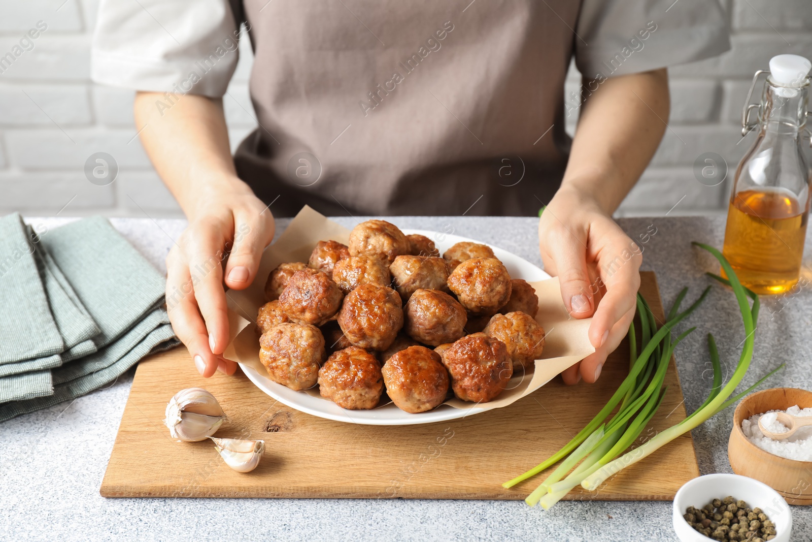 Photo of Woman holding plate with delicious meatballs at light textured table, closeup