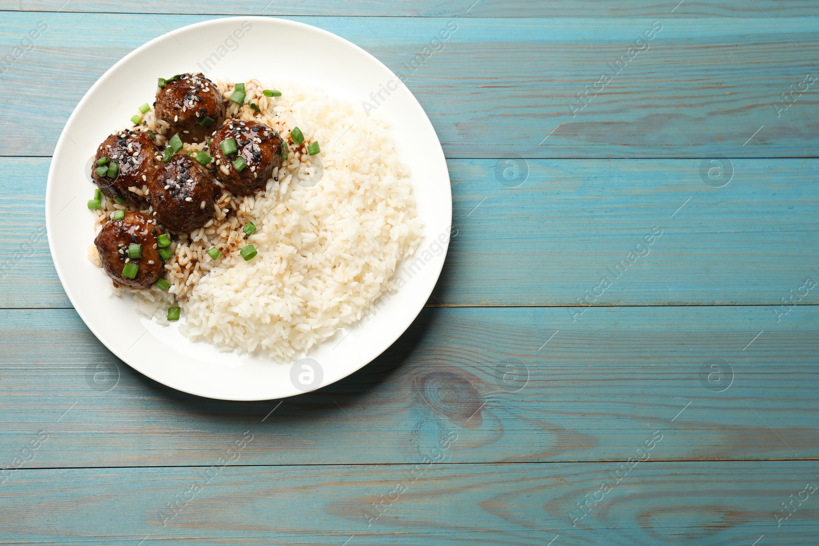 Photo of Delicious rice with meatballs, sauce and green onions on blue wooden table, top view. Space for text