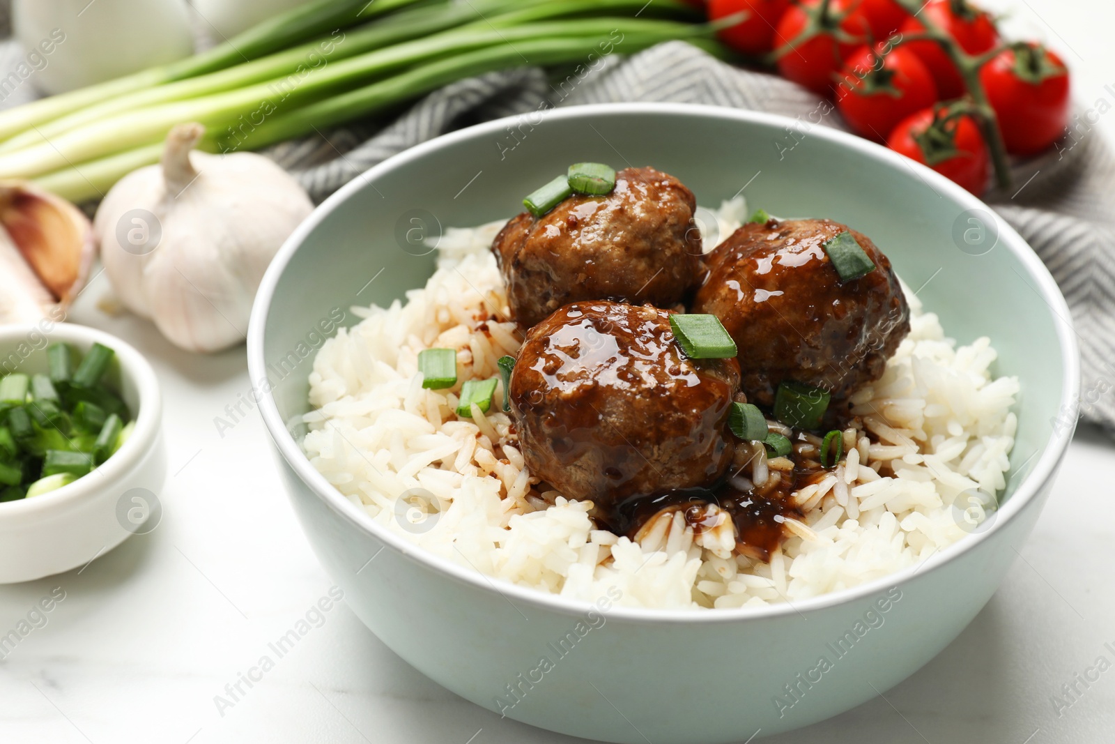 Photo of Delicious rice with meatballs, sauce and green onions on white marble table, closeup