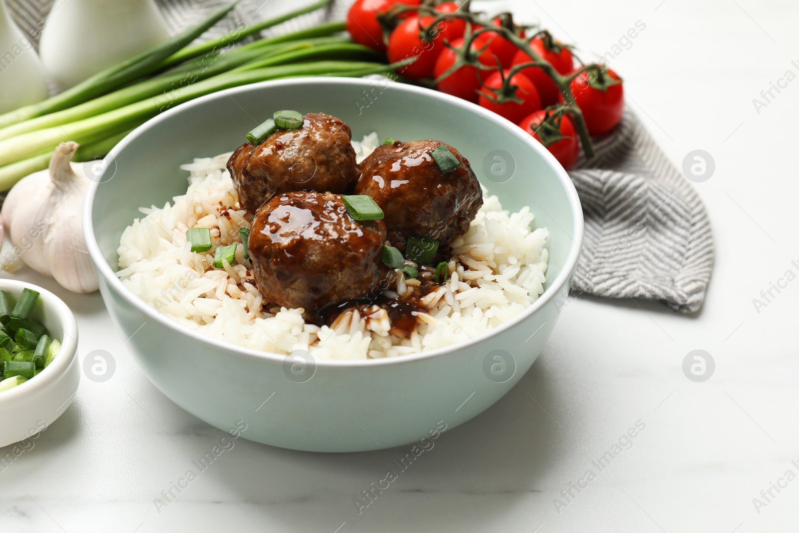 Photo of Delicious rice with meatballs, sauce and green onions on white marble table, closeup