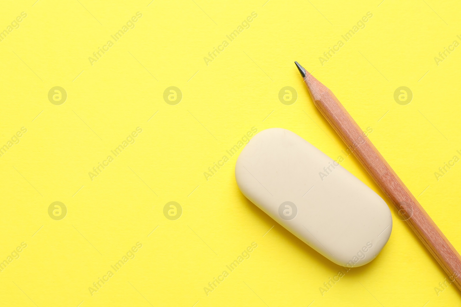 Photo of Eraser and pencil on yellow background, top view. Space for text