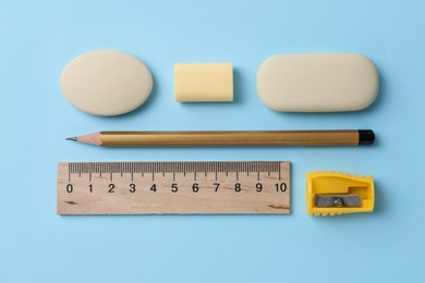 Photo of Erasers and other stationery on light blue background, flat lay