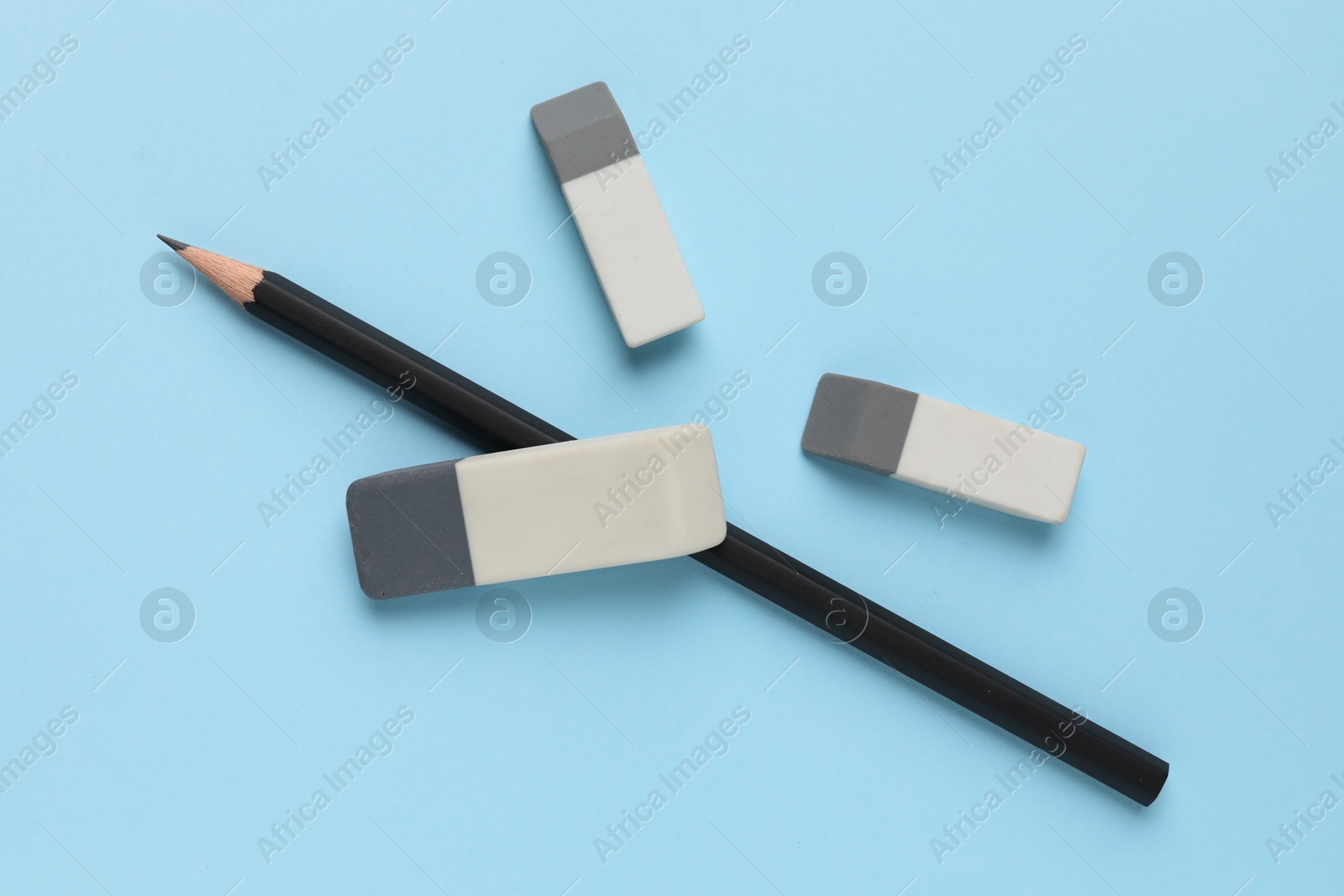 Photo of Erasers and pencil on light blue background, top view