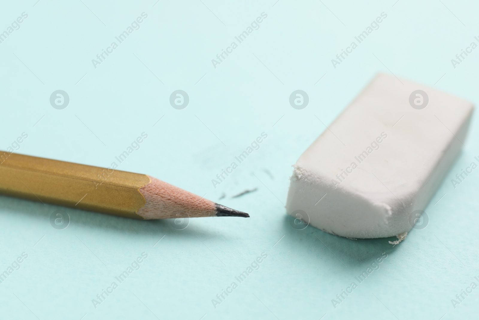 Photo of Eraser and pencil on light blue background, closeup