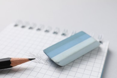 Photo of Eraser, pencil and notepad on light background, closeup