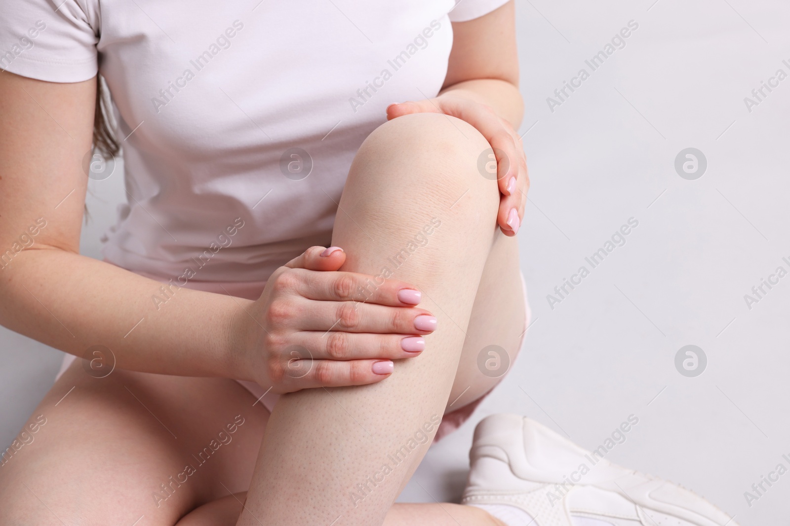 Photo of Young woman suffering from pain in knee on light grey background, closeup