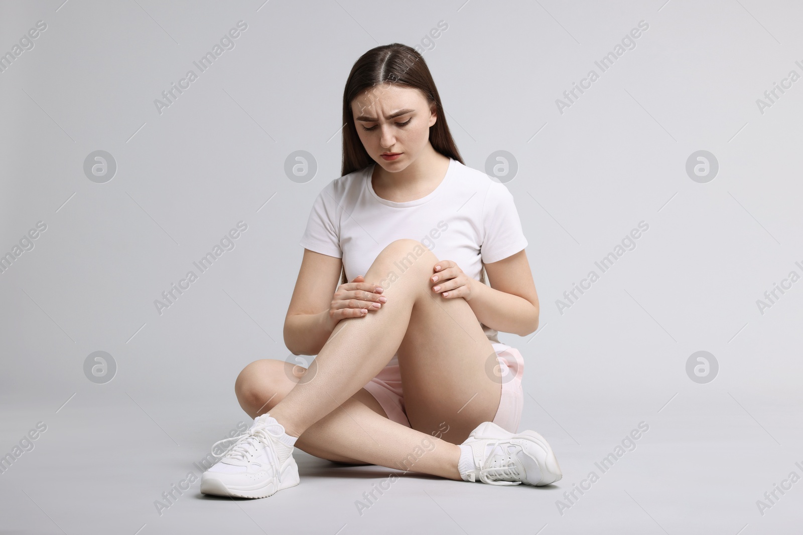 Photo of Young woman suffering from pain in knee on light grey background