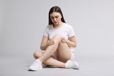 Photo of Young woman suffering from pain in knee on light grey background