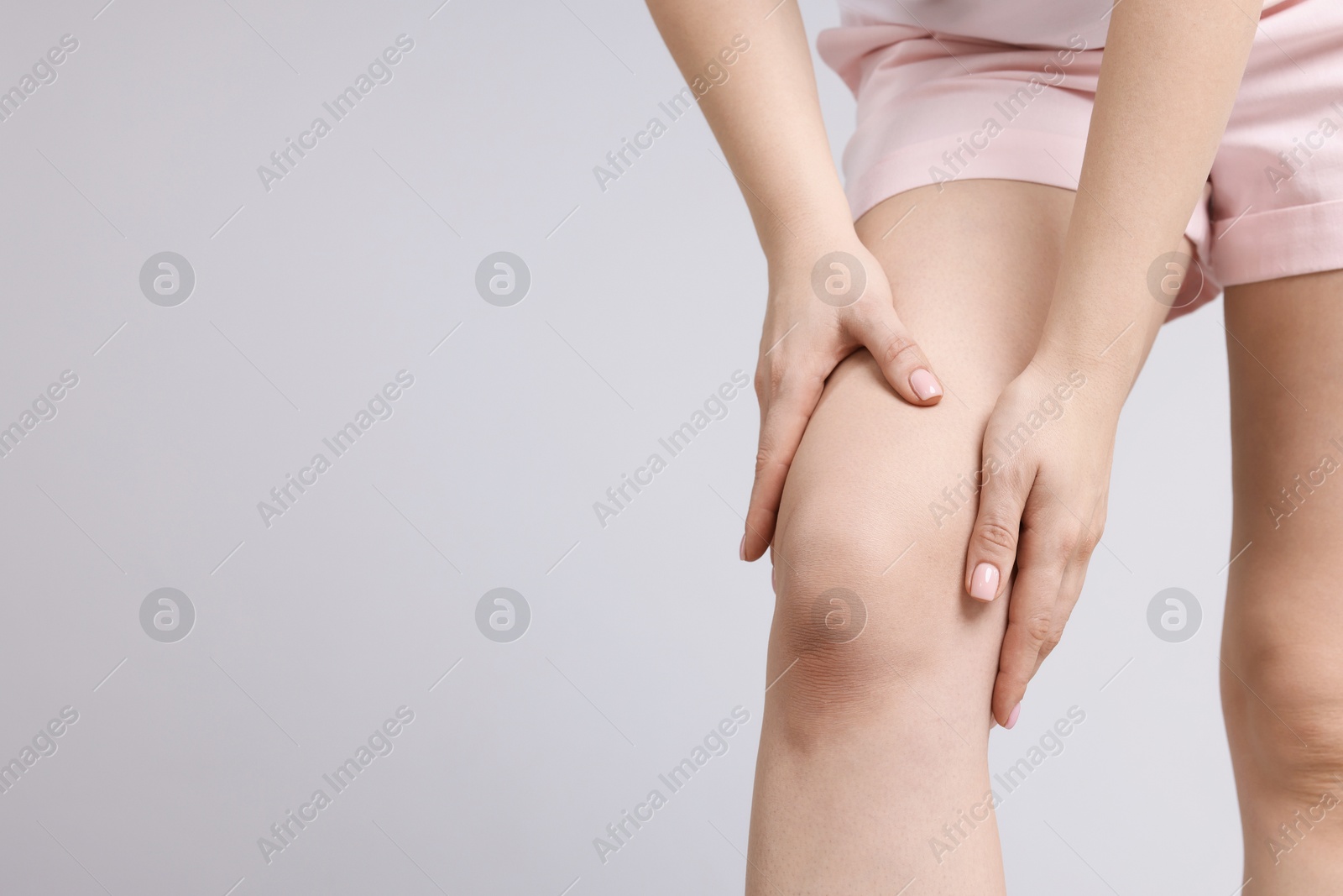 Photo of Young woman suffering from pain in knee on light grey background, closeup. Space for text