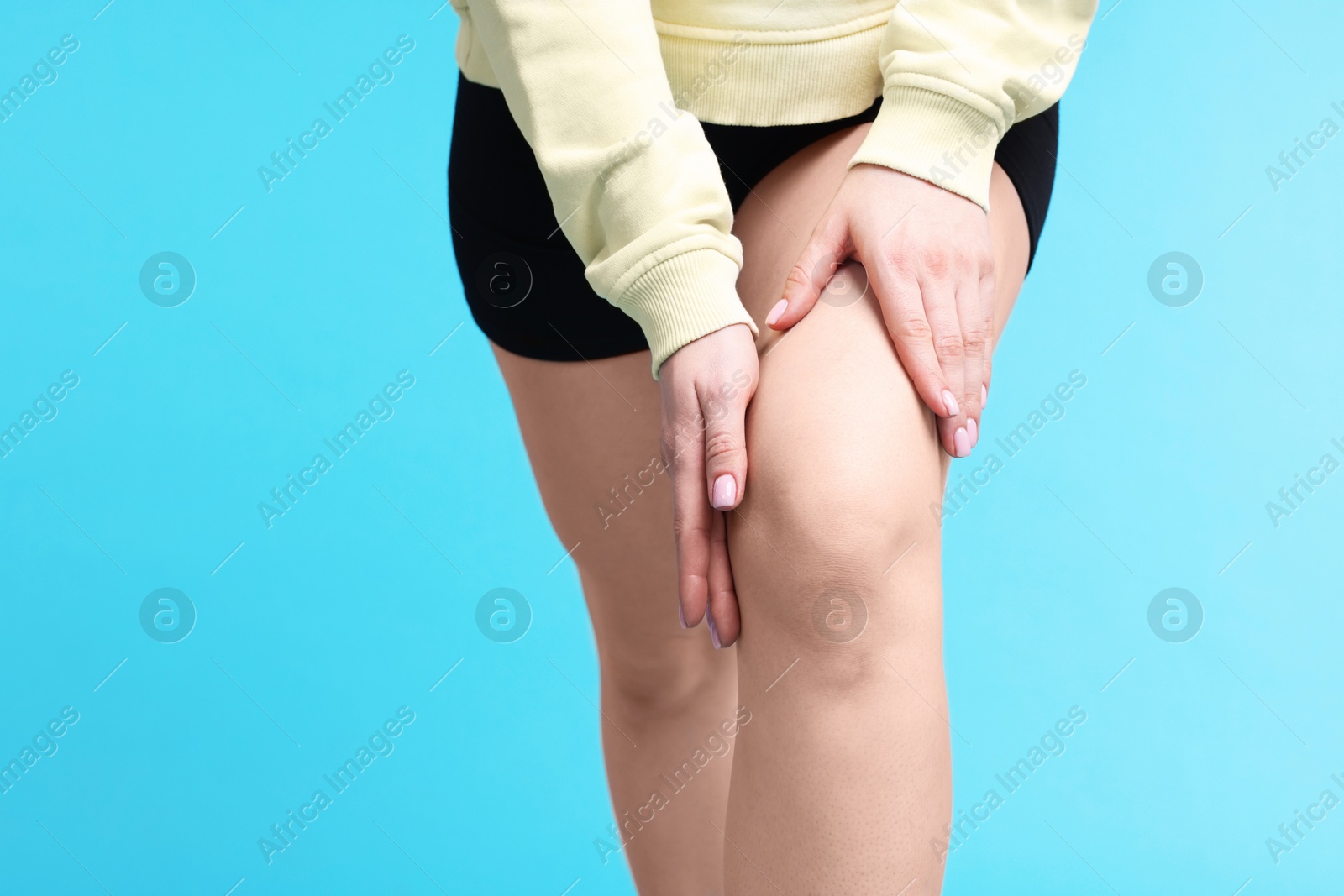 Photo of Young woman suffering from pain in knee on light blue background, closeup