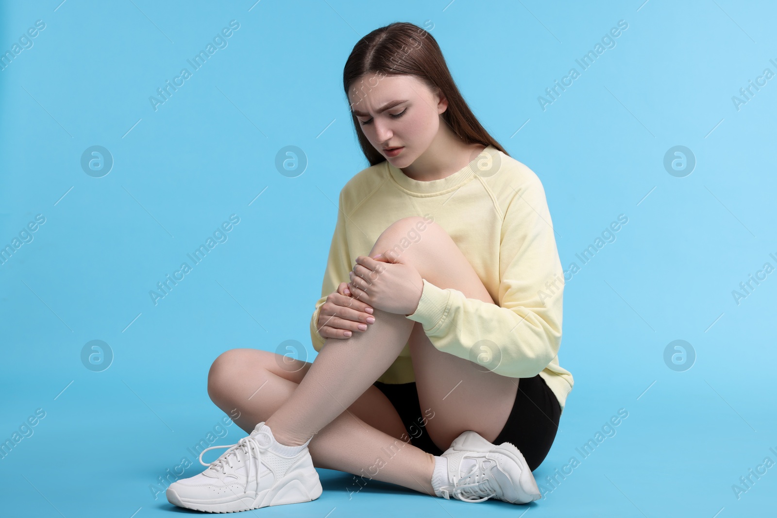 Photo of Young woman suffering from pain in knee on light blue background