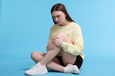 Photo of Young woman suffering from pain in knee on light blue background