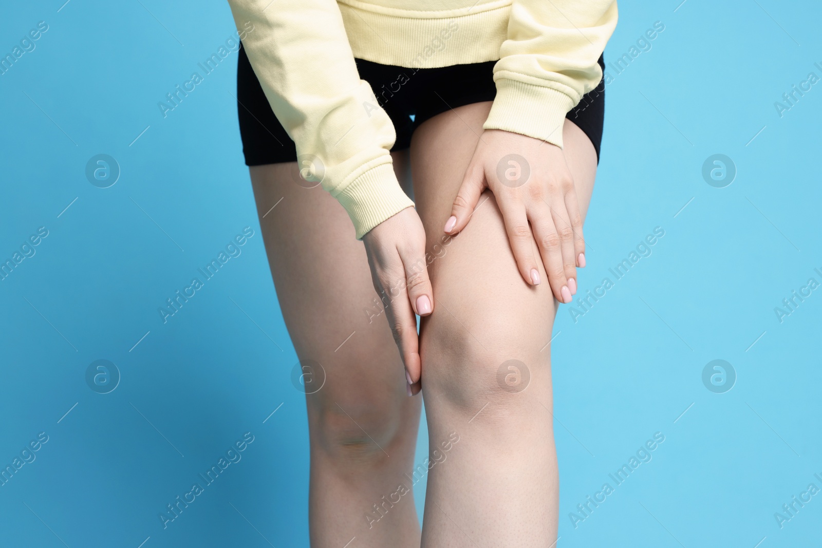 Photo of Young woman suffering from pain in knee on light blue background, closeup