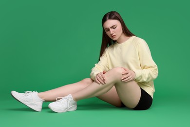 Photo of Young woman suffering from pain in knee on green background